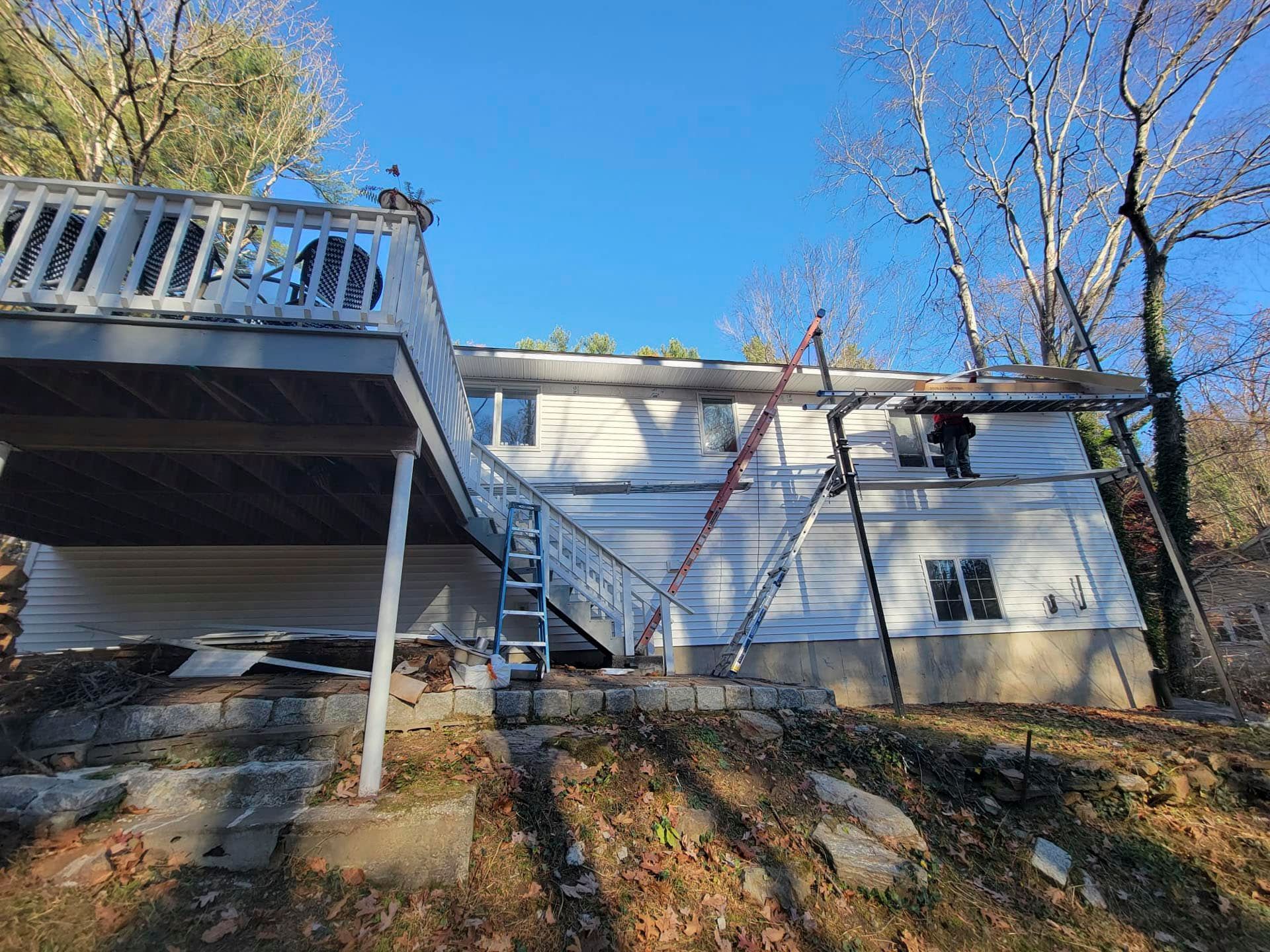 White house with a raised deck and stairs on a wooded hillside under a clear blue sky
