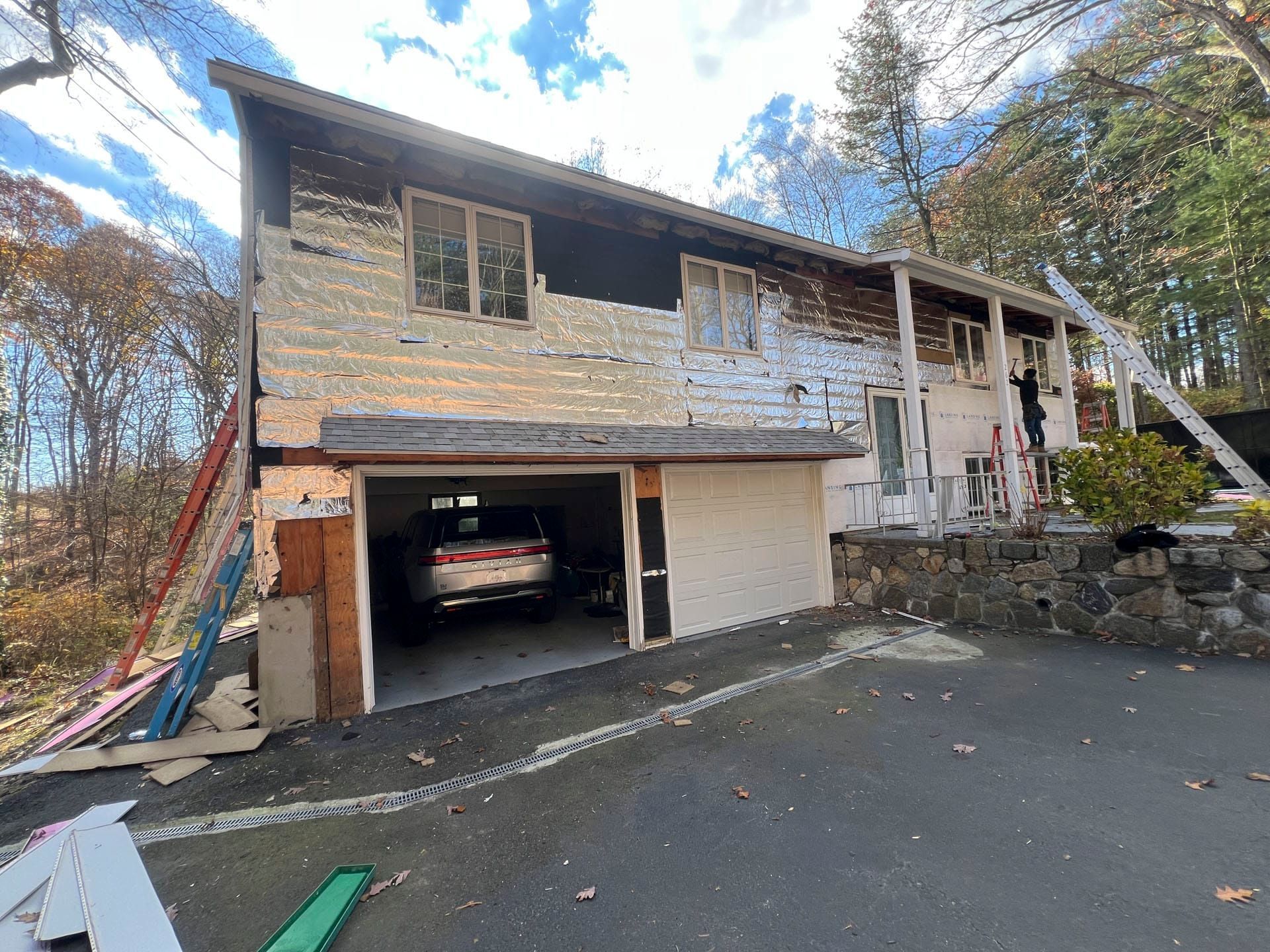 Damaged two-story house with burned exterior, open garage, and debris on the driveway