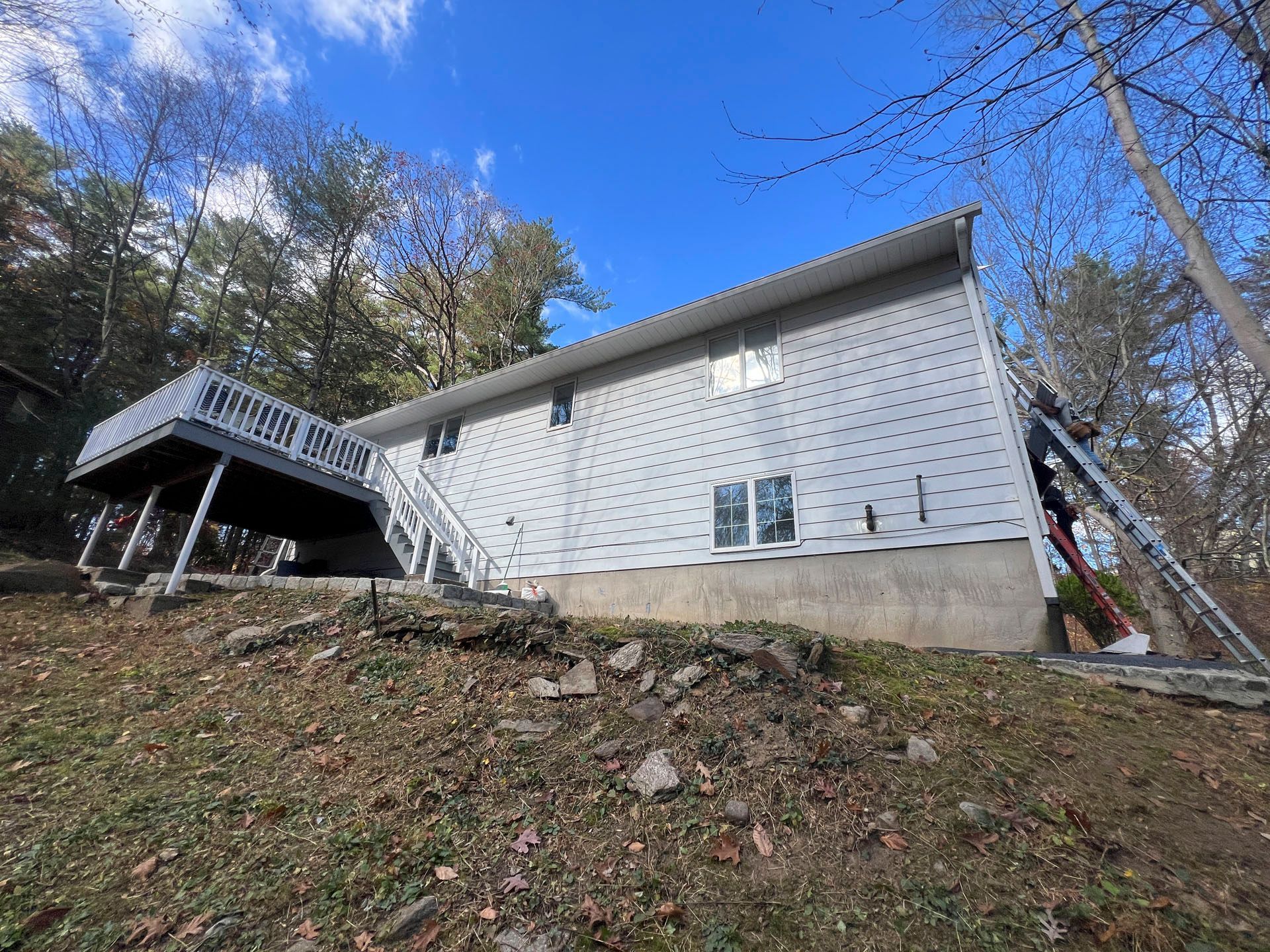 Side view of a white house on a wooded slope with a stair ramp and concrete foundation