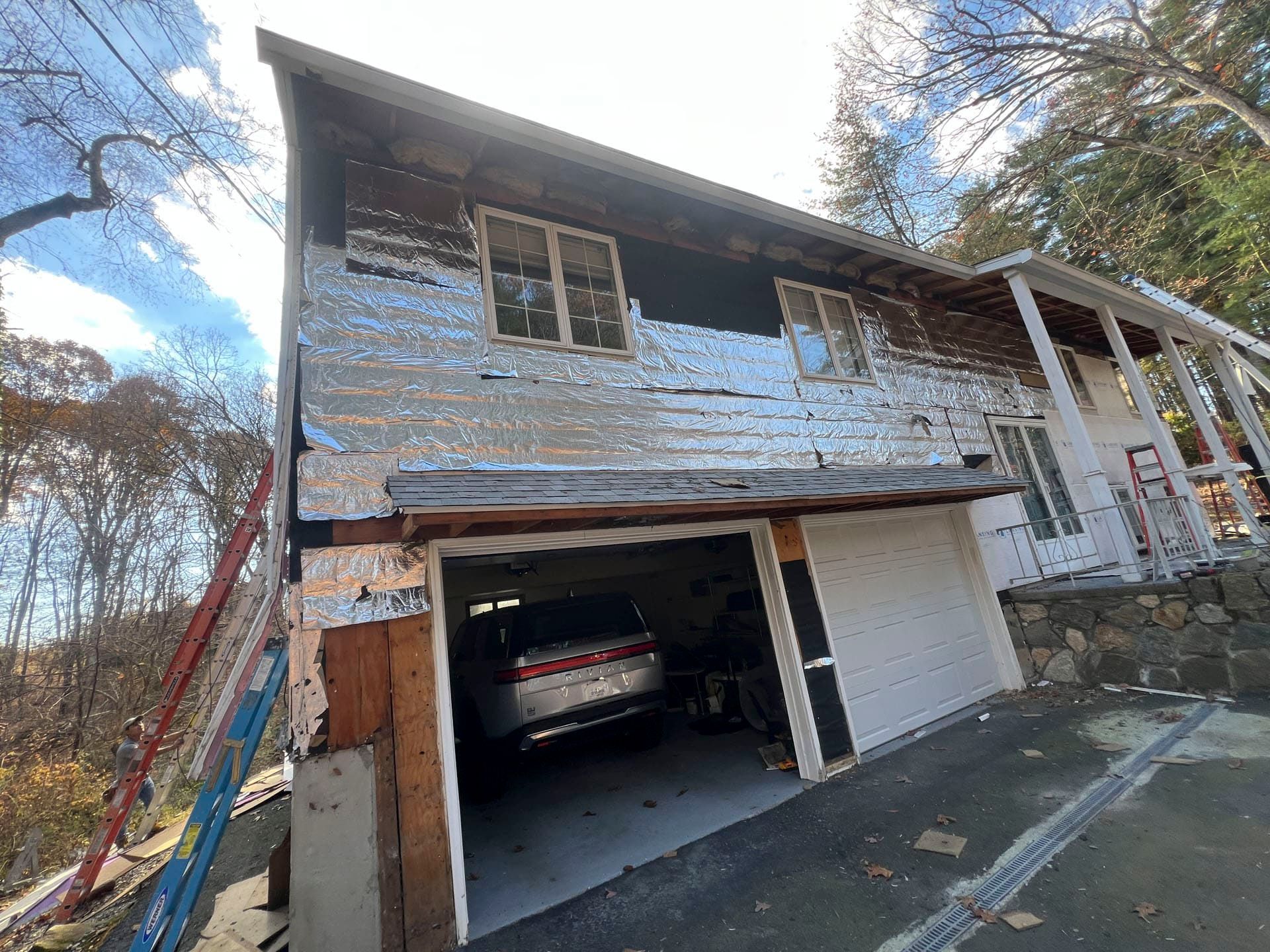Weathered two-story house with an open garage and a car parked inside, viewed from the driveway.