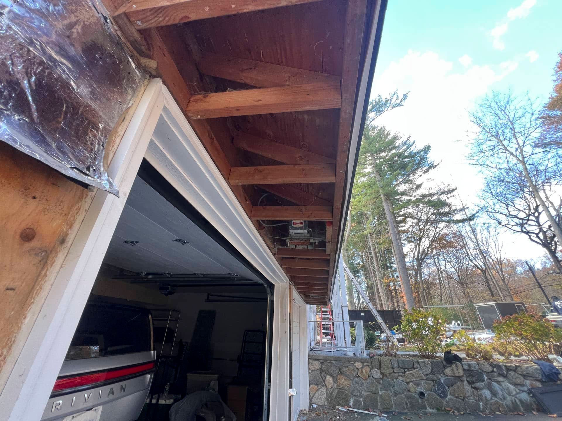 Open garage with wooden overhang and stone wall, viewed from driveway on a sunny day