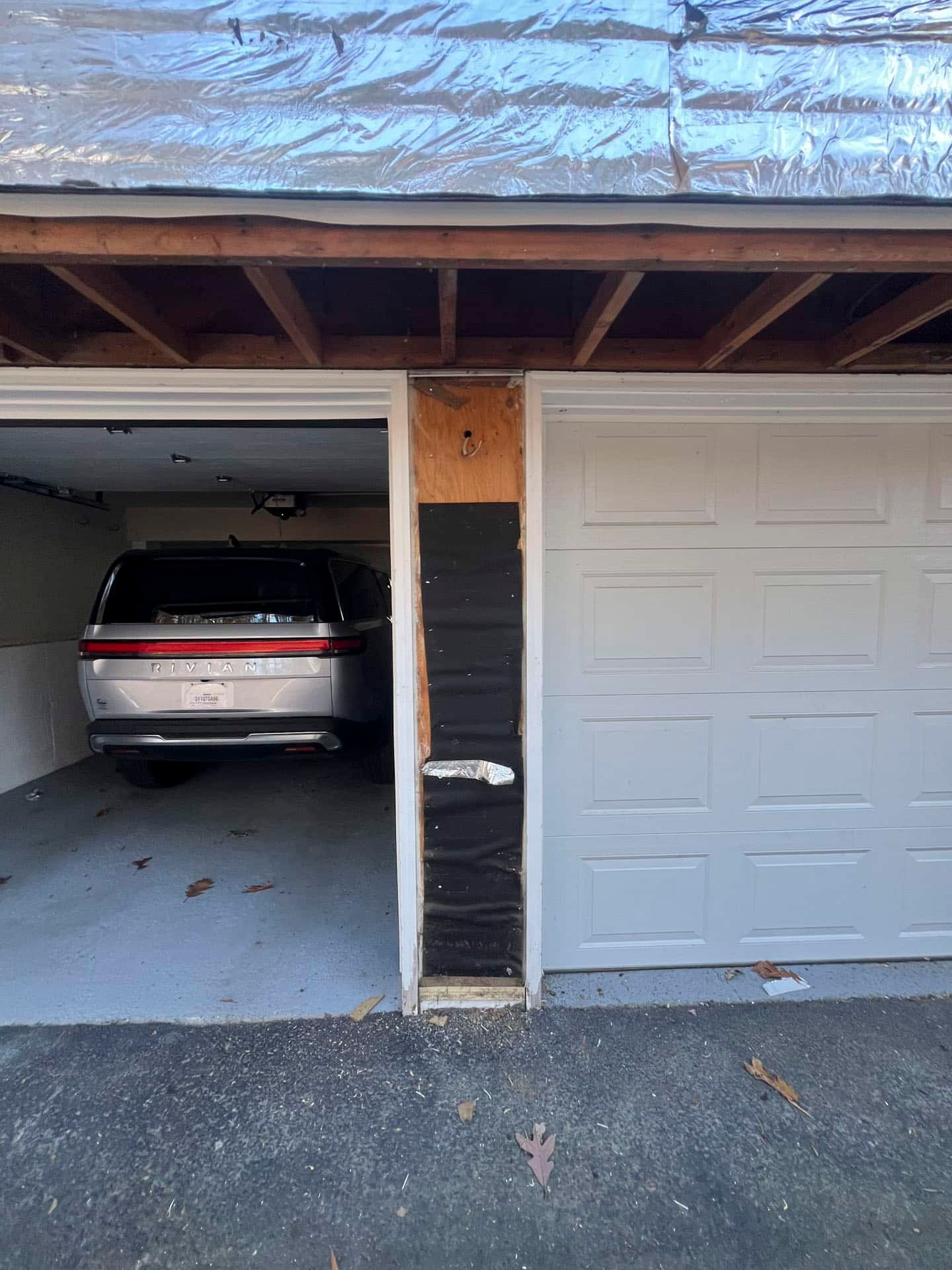 Damaged garage doorway with exposed framing, split between parked SUV and closed white garage door
