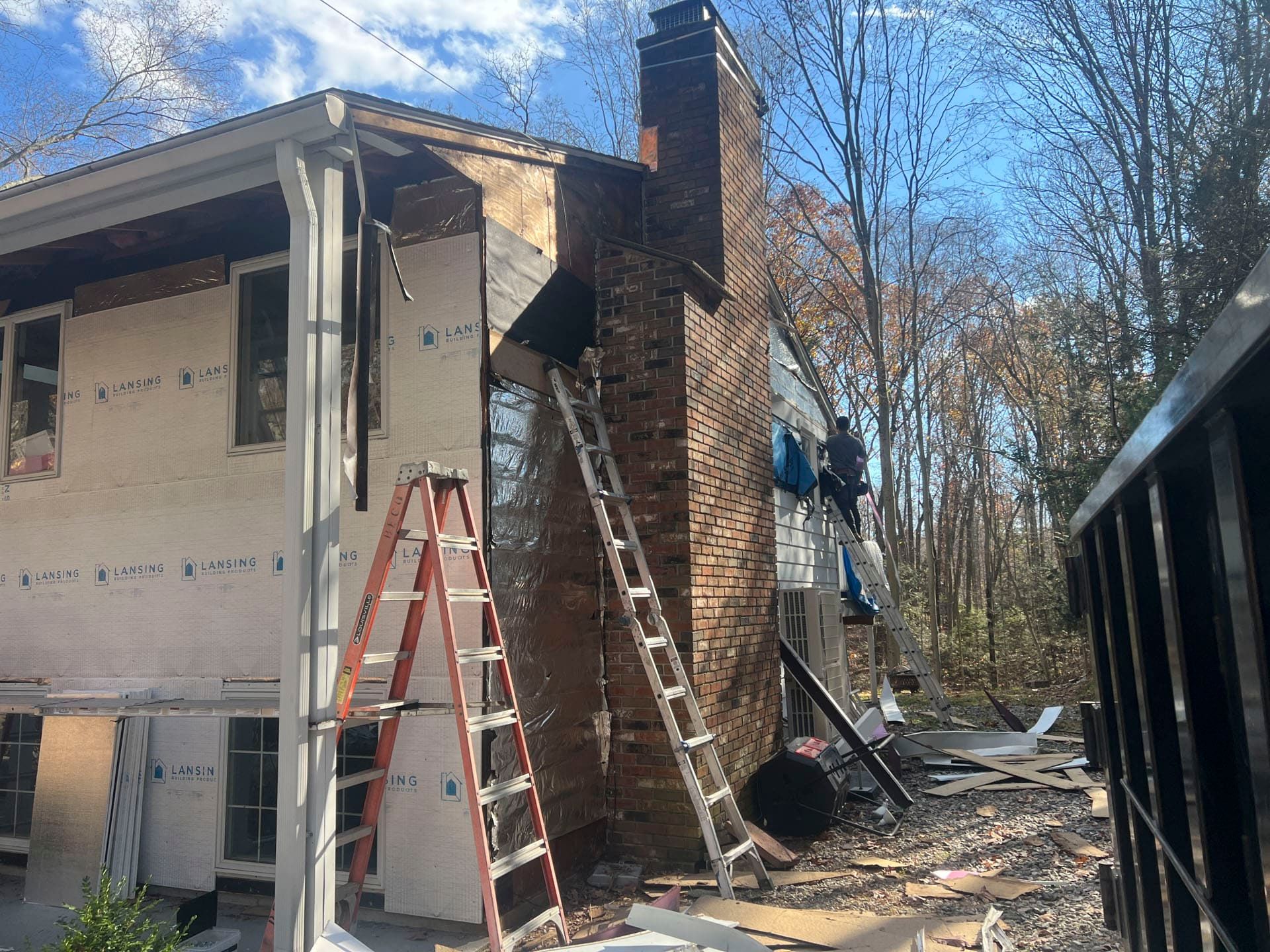 House exterior under repair with ladders, exposed brick chimney, and construction debris outside.