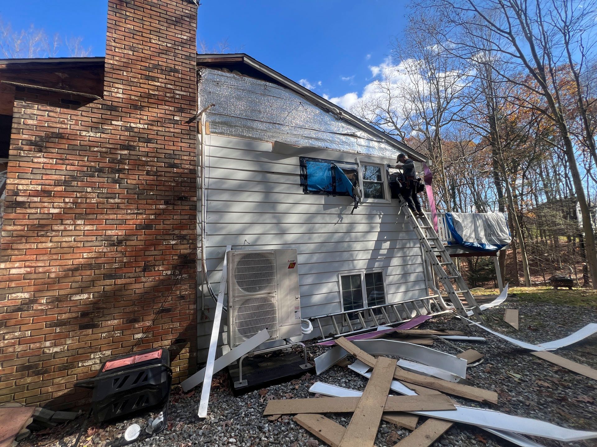 Damaged house exterior with broken windows, debris, and a torn tarp after storm damage