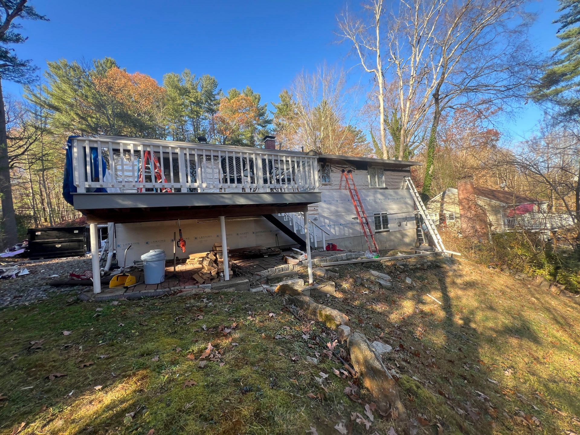 Rustic cabin with a covered deck on a wooded hillside under a bright blue sky