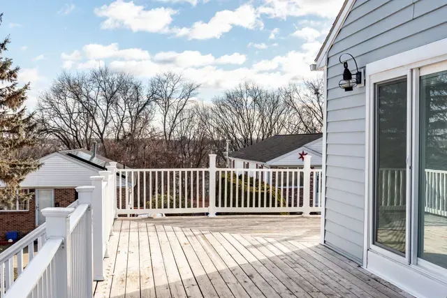 Wooden deck with white railing, light blue house exterior, and view of bare trees under a cloudy sky.