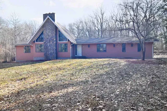 A large house is sitting on top of a lush green field surrounded by trees .