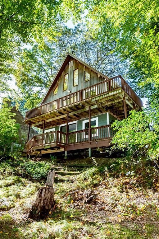 Cabin nestled among green trees, with two levels of brown decks and a stair leading up.