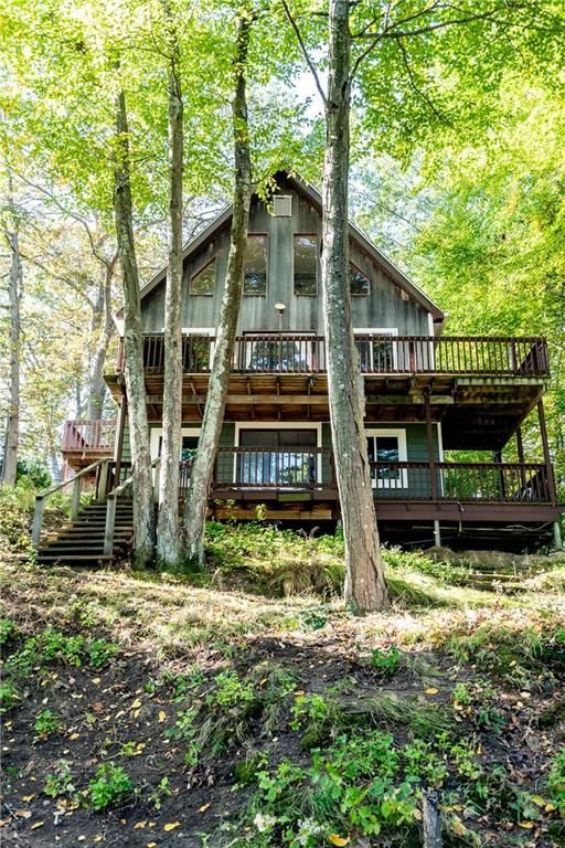 Two-story cabin nestled among trees, with a wraparound deck and stairs.