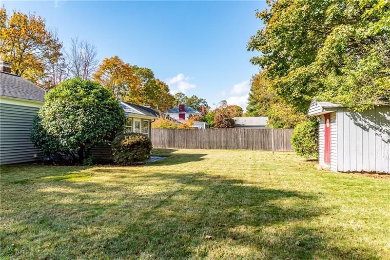 Grassy backyard with wooden fence and small outbuildings, under a blue sky.