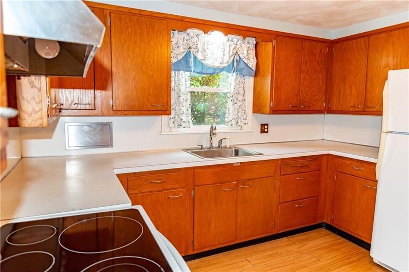 Kitchen with wooden cabinets, white countertops, and an electric stove. A window with a curtain is above the sink.