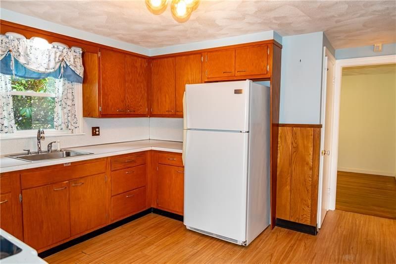 Kitchen with wood cabinets, white fridge, and a sink by a window with a valance.