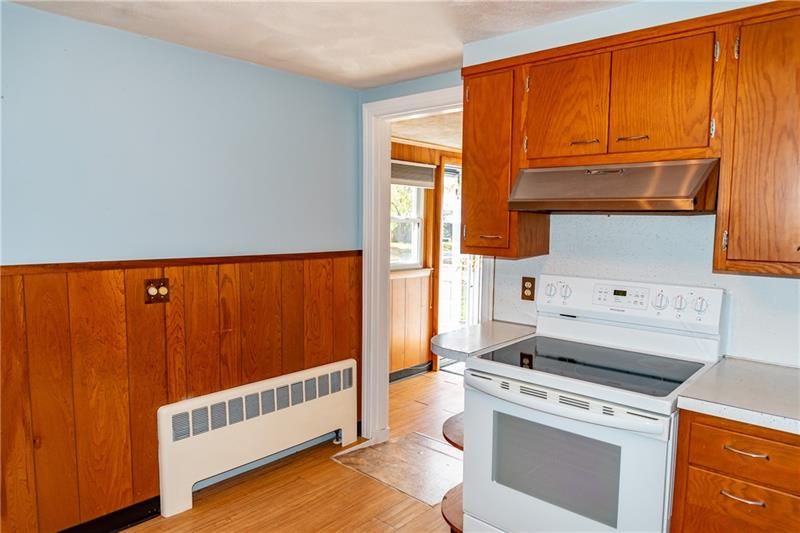 Kitchen with wood paneling, light blue walls, white stove, and wooden cabinets. Doorway leads to outside.
