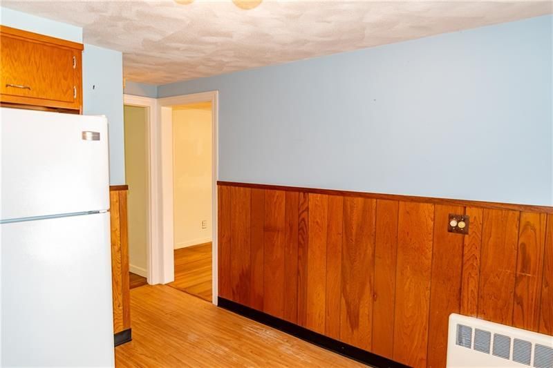 Kitchen with light blue wall, wood paneling, white refrigerator, doorway, and light wood flooring.