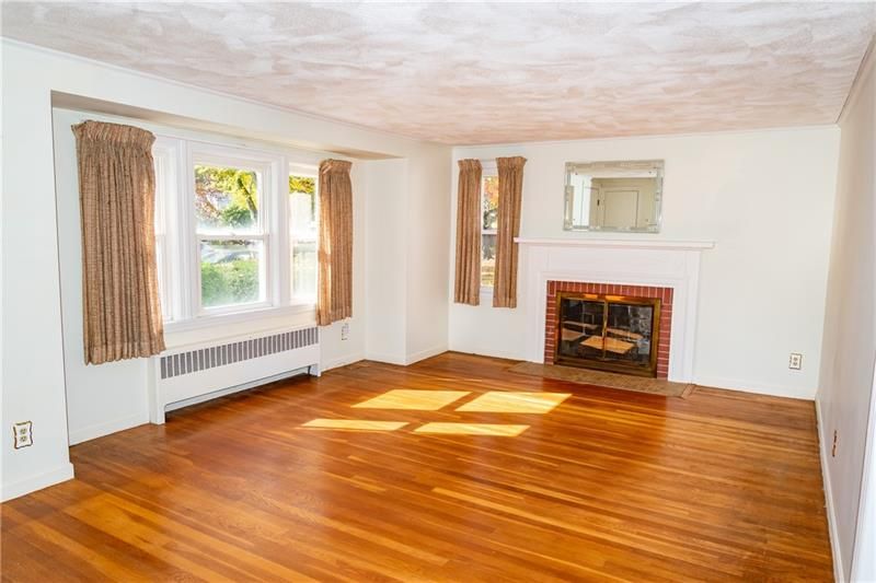 Empty living room with hardwood floors, fireplace, and window with curtains.