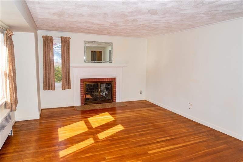 Empty living room with hardwood floors, a fireplace, and a window with curtains.