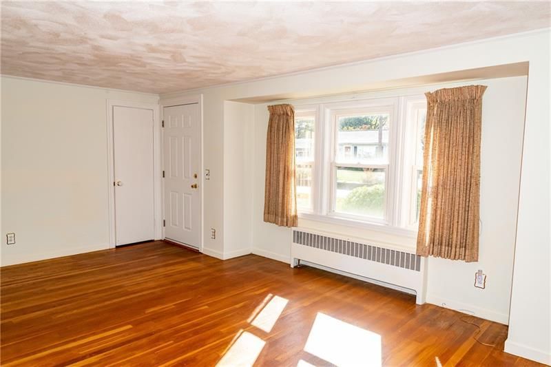 Empty room with hardwood floors, a bay window with curtains, and two doors.