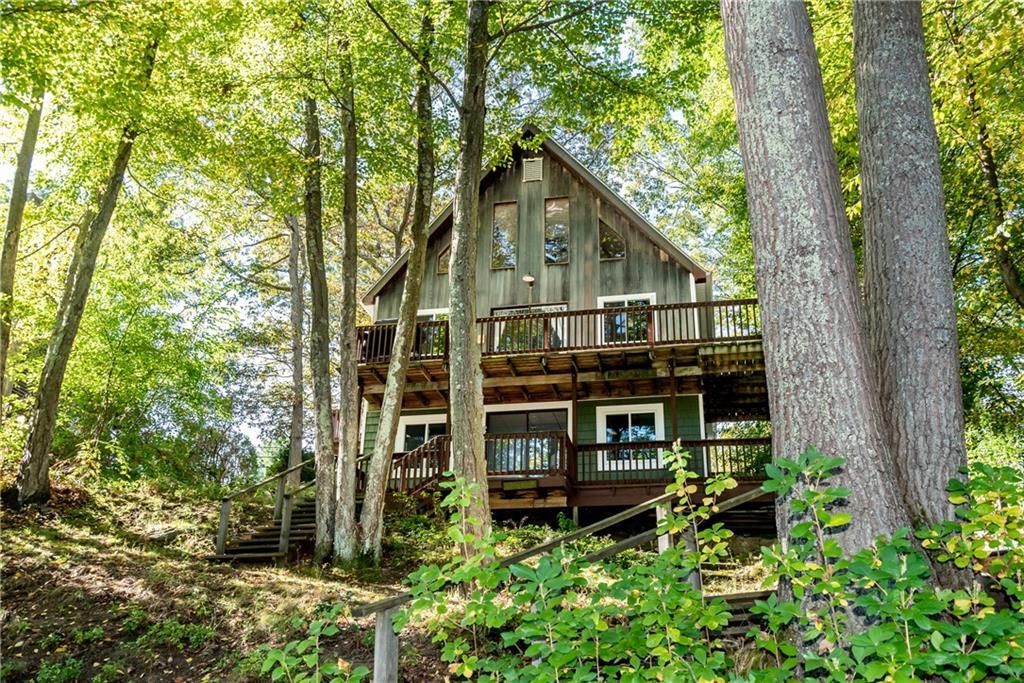 Two-story cabin nestled among trees, with a deck and weathered wood siding.