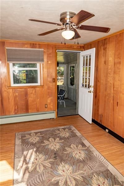 Room with wood-paneled walls, a rug, a window with a shade, and a door leading outside. Ceiling fan present.