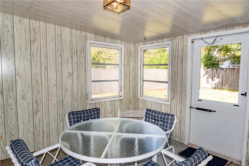 Sunroom with white paneling, glass table, blue and white chairs, two windows, and a door to the outside.