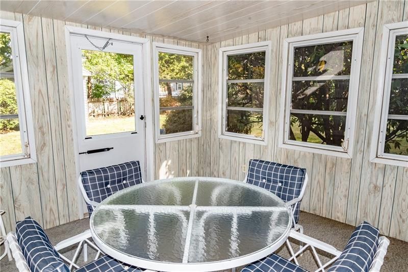 Sunroom with glass table and chairs, windows overlooking a yard.