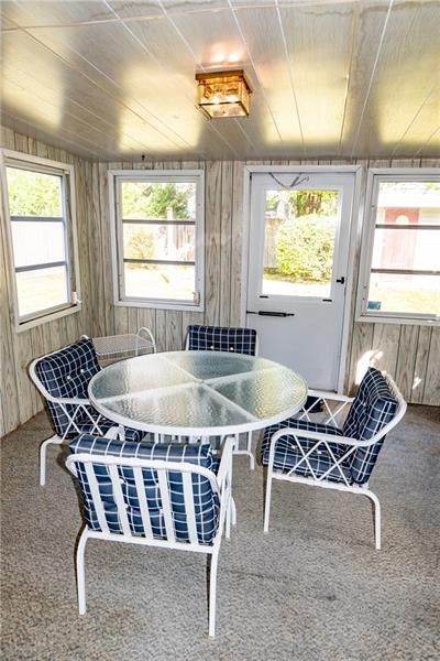 Sunroom with a round glass table and four blue and white chairs; several windows and a door.