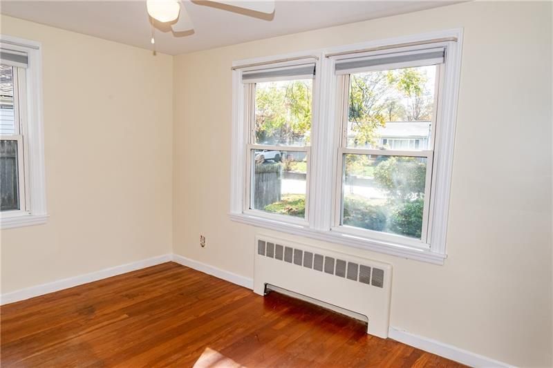 Empty room with wood floors, two windows, radiator, and a ceiling fan.