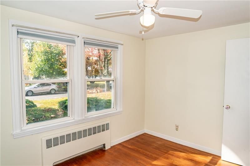 Empty bedroom with two windows, a white door, hardwood floor, and a ceiling fan.