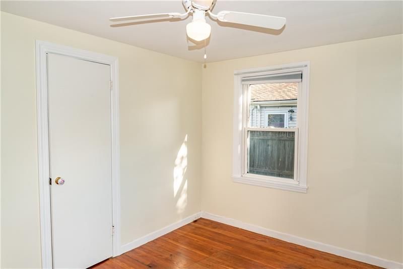 Empty bedroom with white walls, a closed door, window, ceiling fan, and hardwood floors.