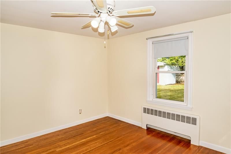Empty bedroom with wood floor, beige walls, ceiling fan, and window overlooking a yard.