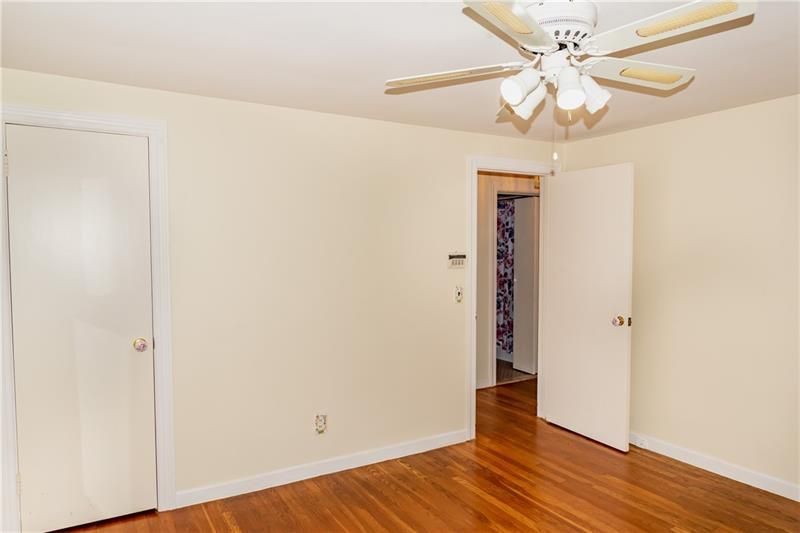 Empty bedroom with wood floors, two white doors, open doorway to another room, ceiling fan.