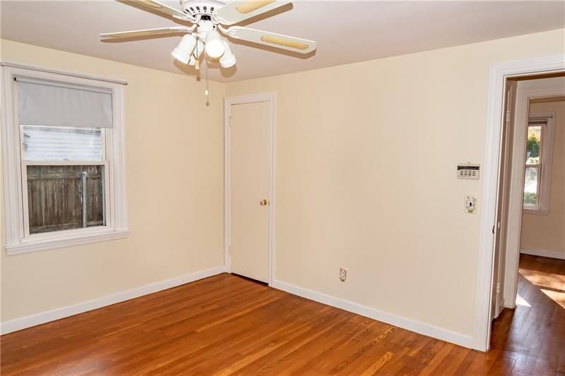 Empty bedroom with light yellow walls, hardwood floors, a closet, window, and a ceiling fan.