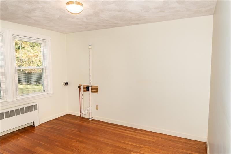 Empty room with hardwood floors, a window, radiator, and unfinished wall plumbing.