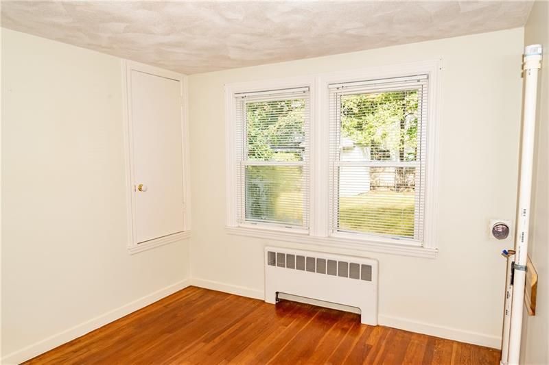 Empty room with hardwood floors, two windows with blinds, built-in closet, and a radiator.