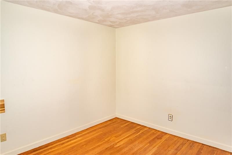 Empty room with light walls, wood floor, and beige textured ceiling. Electrical outlet visible.