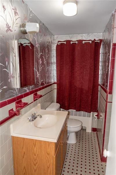Bathroom with floral wallpaper, red trim, and a dark red shower curtain.
