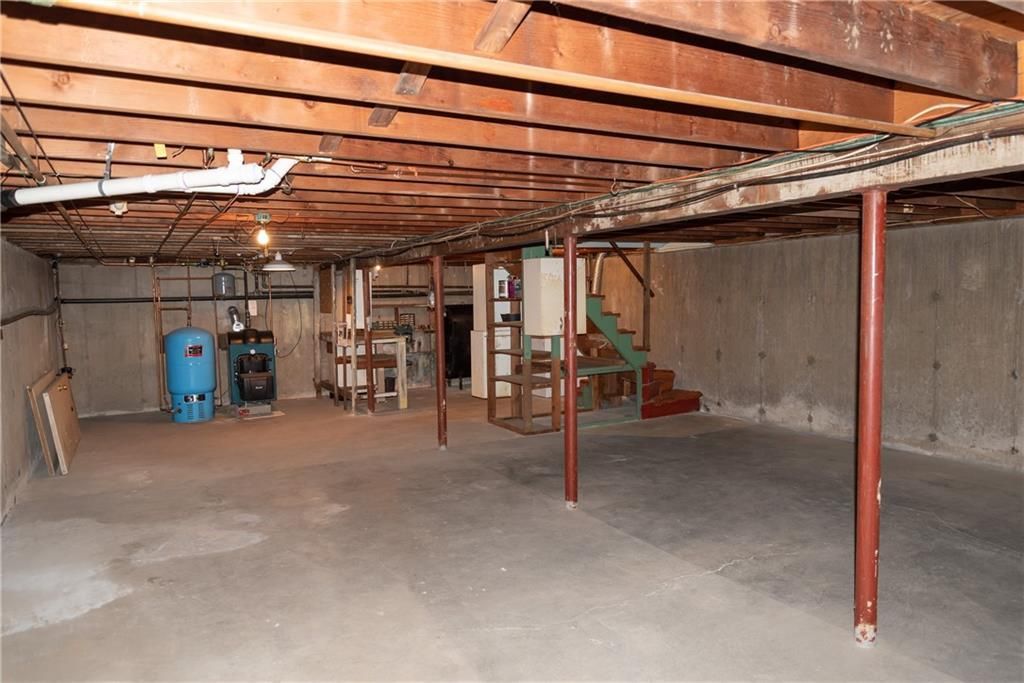 Unfinished basement with concrete floor, exposed ceiling beams, support poles, and utility equipment.