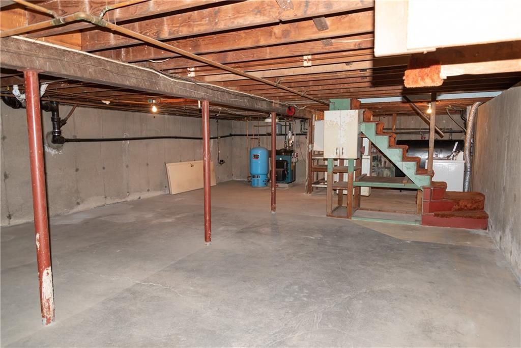 Basement interior with concrete floor, support beams, stairs, and water heater.