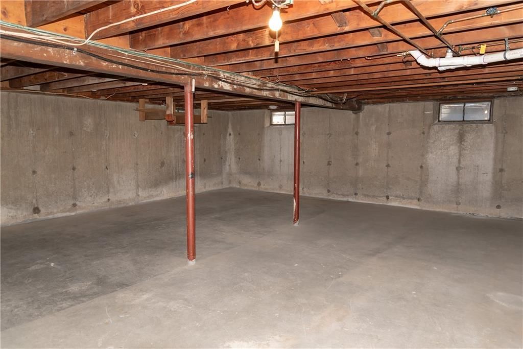Empty basement with concrete floor, walls, exposed wooden ceiling, metal support beams.