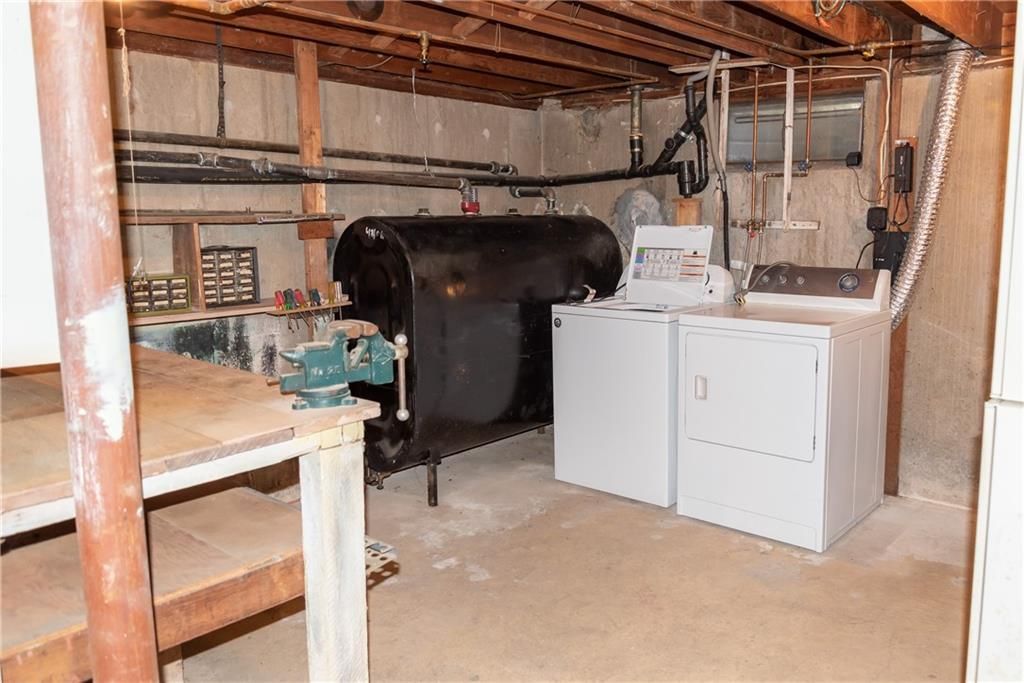Basement with oil tank, washer, dryer, and workbench. Concrete floor and wooden ceiling.