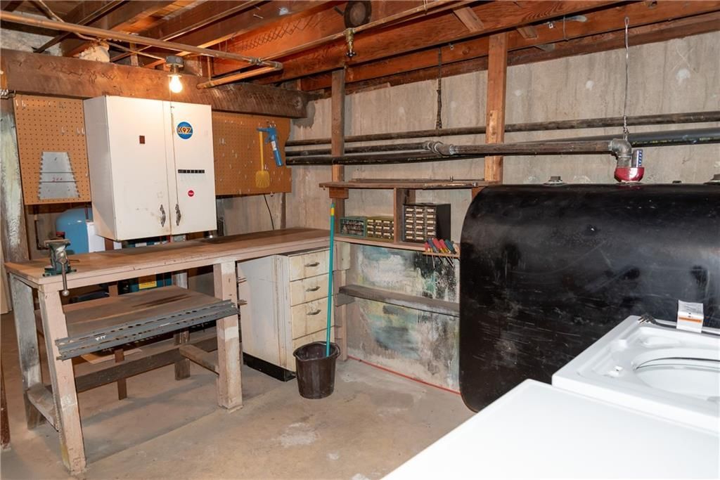 Workshop with workbench, cabinets, and oil tank. Concrete floor, wood beams, and various tools.