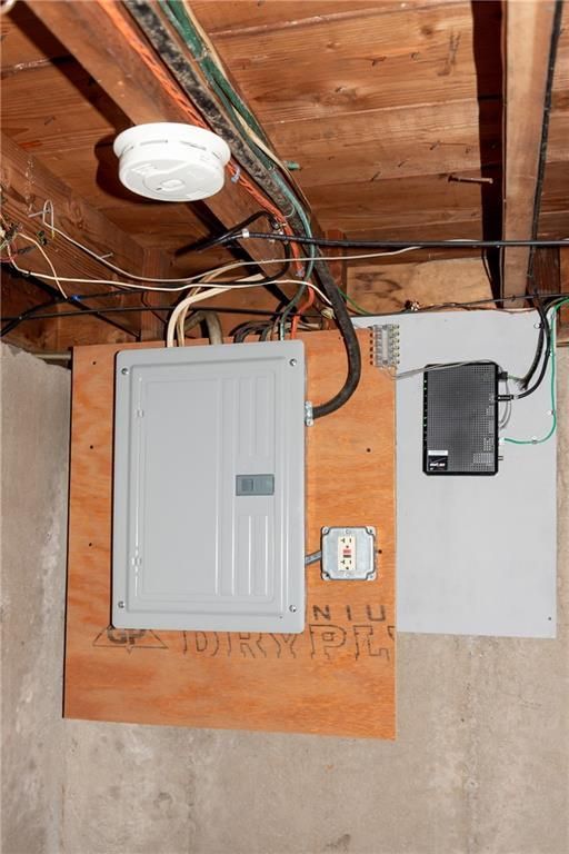 Electrical panel and network box mounted on wood in a basement, with exposed wires and a smoke detector.