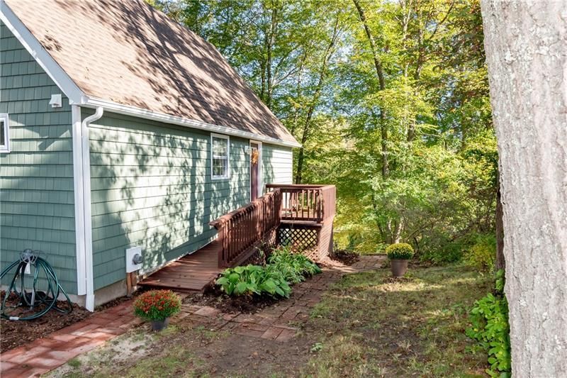 Green house with brown roof and wooden deck surrounded by trees.
