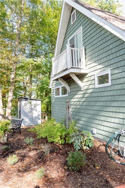 Green shingled house with a balcony, surrounded by trees and a garden.