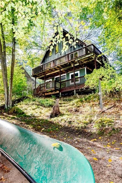 Two-story cabin with decks, surrounded by trees. A green canoe in the foreground.