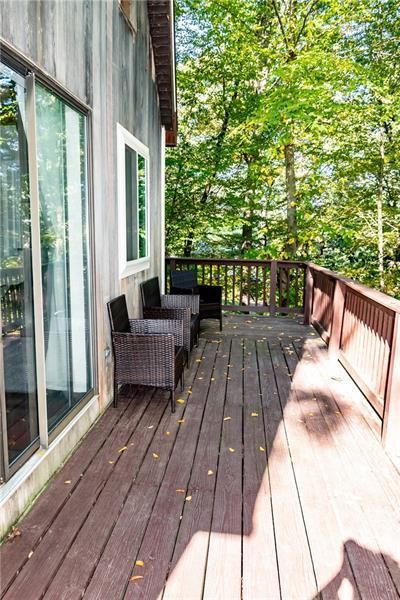 Wooden deck with brown chairs overlooking green trees. Gray siding with large windows.