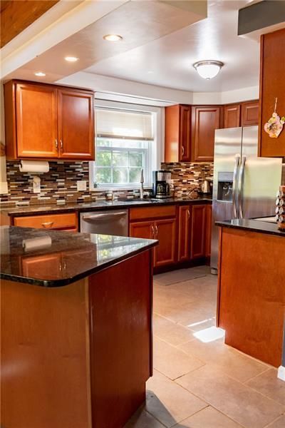 Kitchen with brown cabinets, black countertops, stainless steel appliances, and beige tile floor.