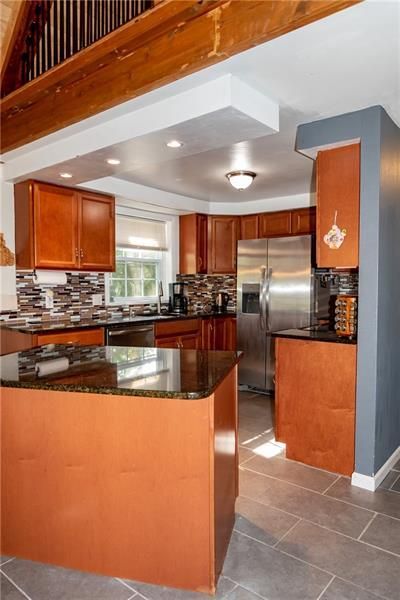 Kitchen with brown cabinets, granite countertops, stainless steel appliances, and gray tile floor.