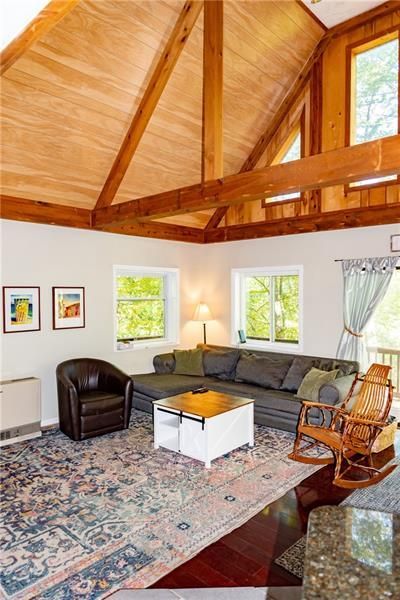 Living room with wood beams, vaulted ceiling, sofa, armchair, rug, windows.