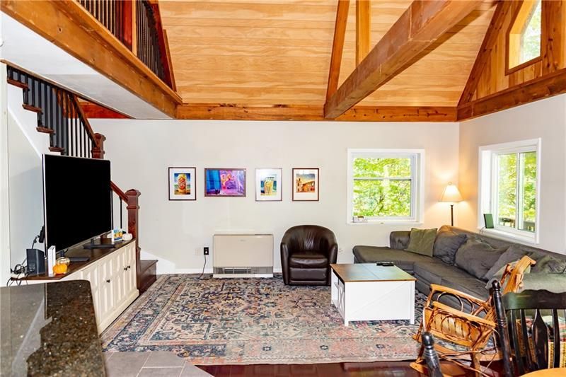 Living room with exposed wood beams, staircase, sofa, TV, rug, and artwork.